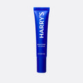Blue tube of Harry's Brightening Eye Cream on a light gray background