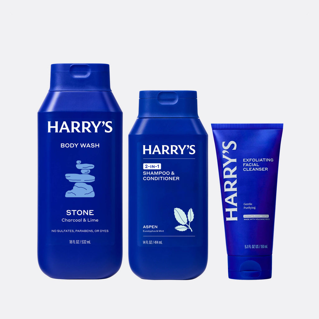 Three blue bottles of Harry's grooming products on a light gray background