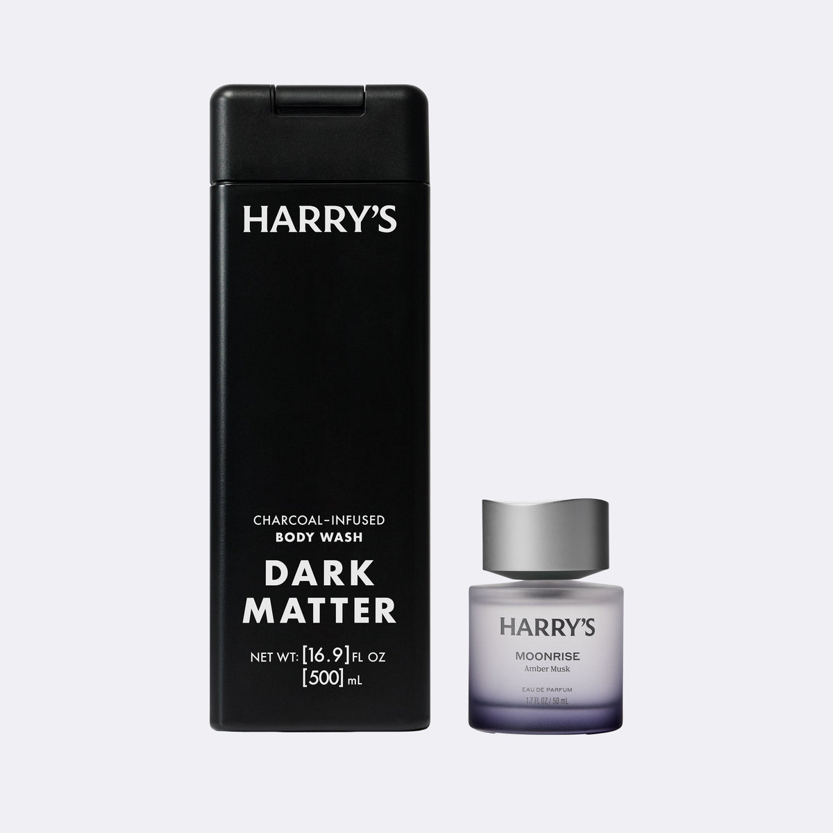 Harry's Dark Matter charcoal-infused body wash shown with its tall black bottle and a smaller Moonrise cologne bottle on a light gray background.