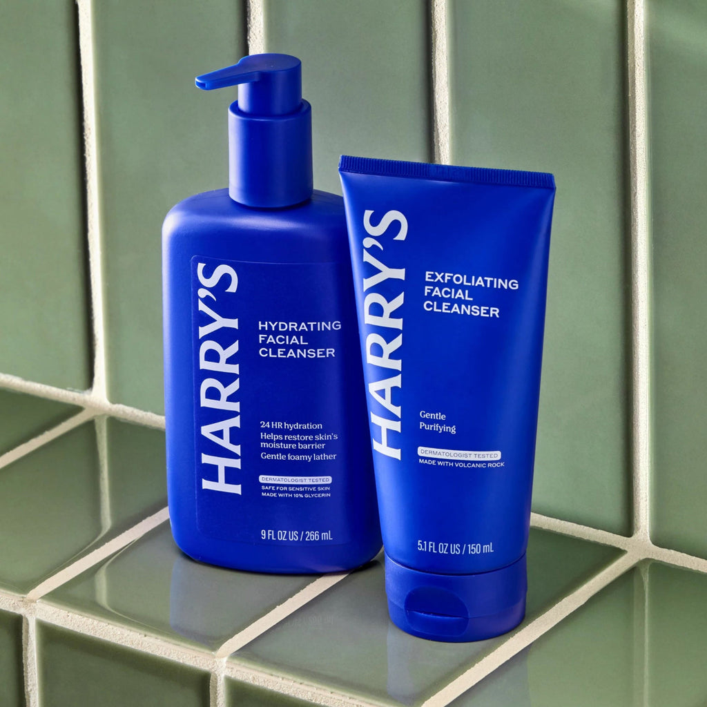Two blue bottles of Harry's facial cleanser on a green tiled surface