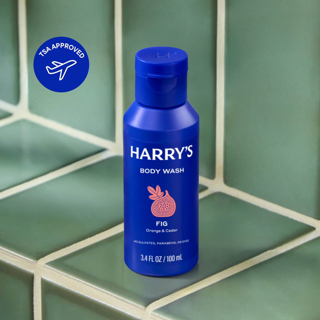 Blue bottle of Harry's body wash on a green tiled surface with TSA Approved logo.