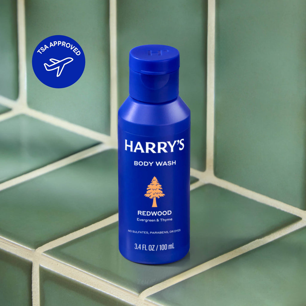 Blue bottle of Harry's body wash on a green tiled surface with TSA Approved logo.
