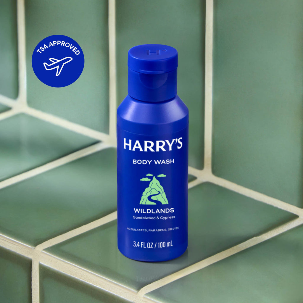 Blue bottle of Harry's body wash on a green tiled surface with TSA Approved logo.