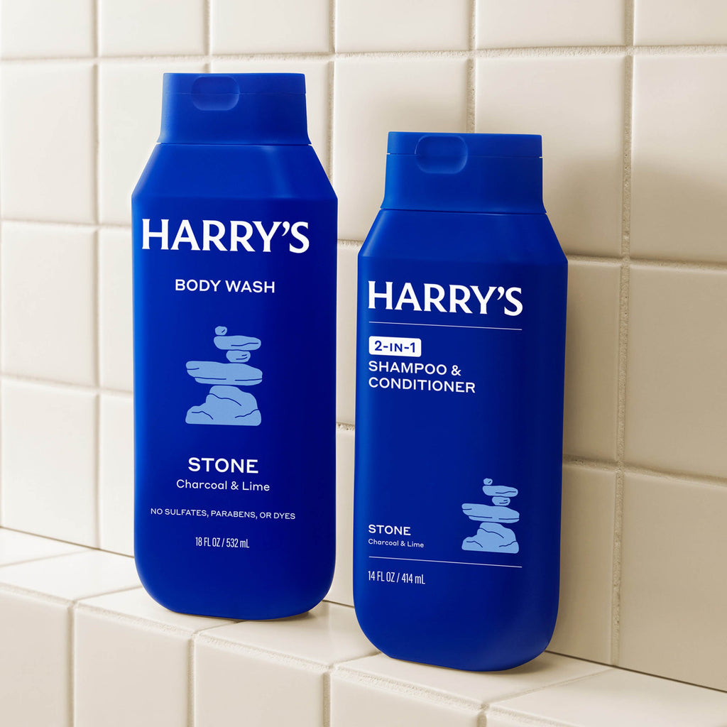 Two blue bottles of Harry's Stone body wash and shampoo & conditioner on tiled shelf