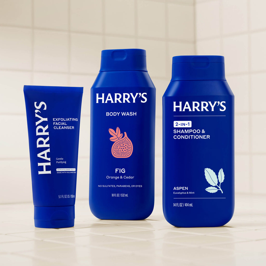 Three blue bottles of Harry's grooming products on a tiled shelf