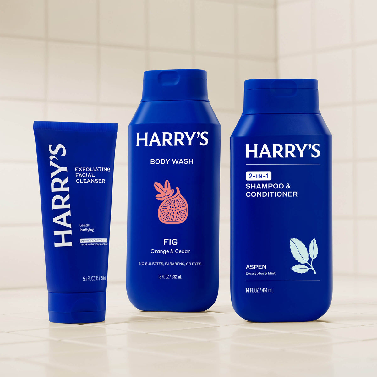 Three blue bottles of Harry's grooming products on a tiled shelf