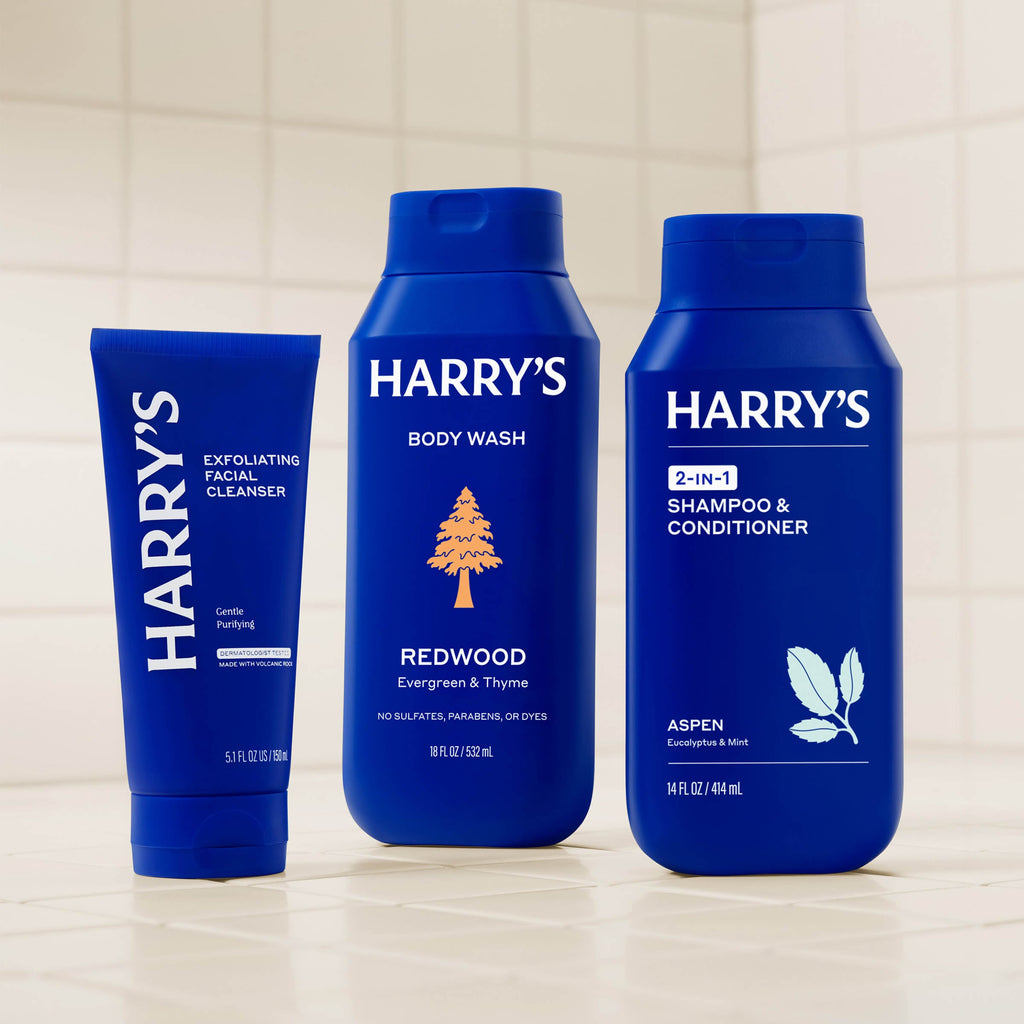 Three blue bottles of Harry's grooming products on a tiled bathroom wall shelf