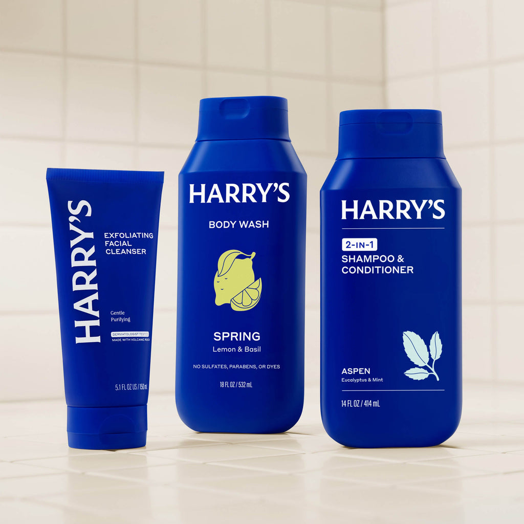 Three blue bottles of Harry's grooming products on a tiled shelf