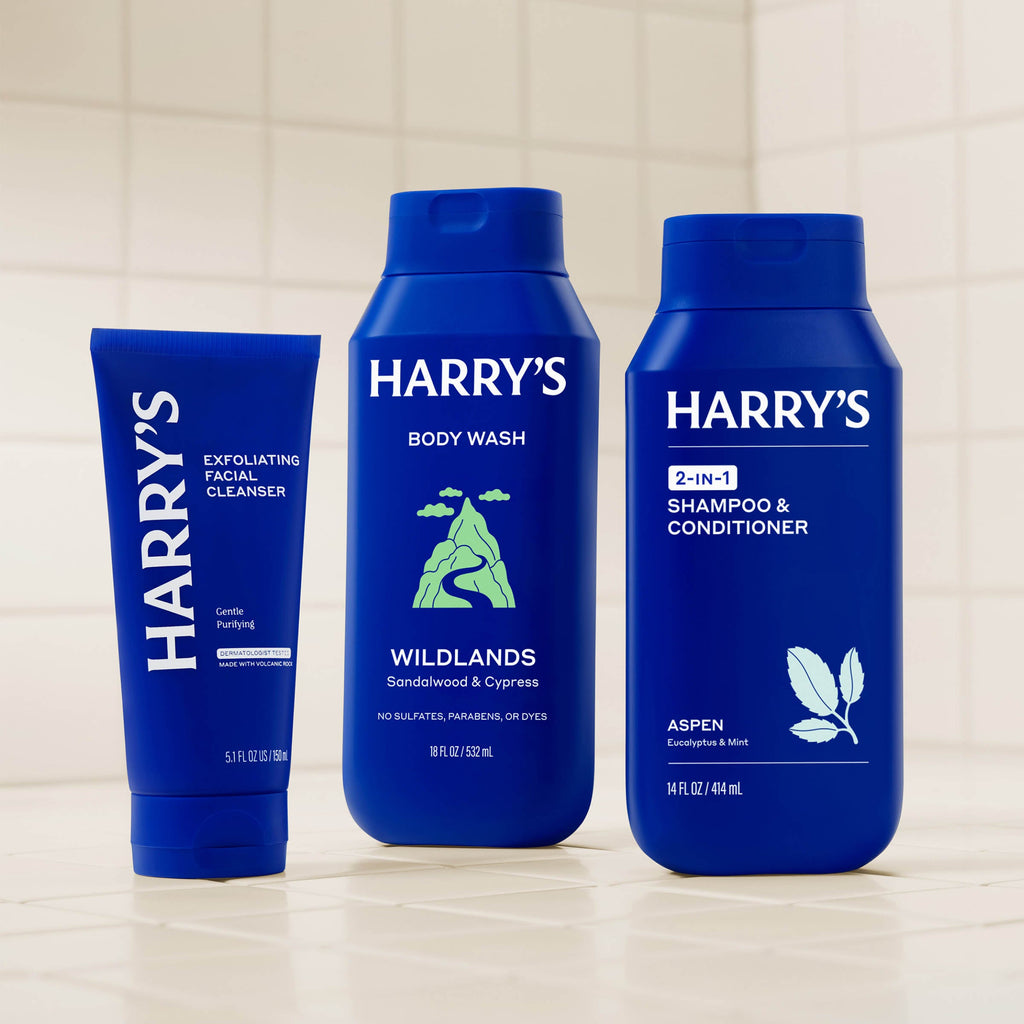 Three blue bottles of Harry's grooming products on a tiled bathroom shelf