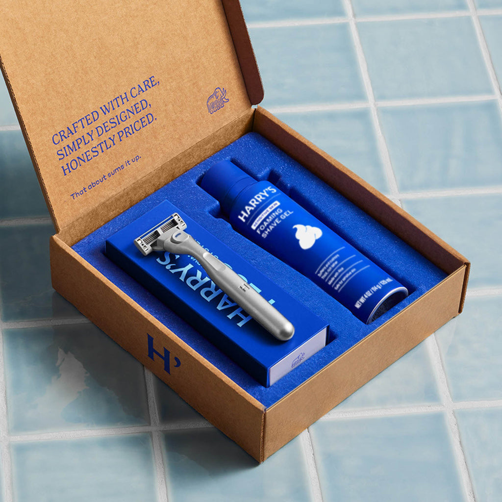 Harry's grooming kit with razor and cream in a cardboard box on a tiled floor.
