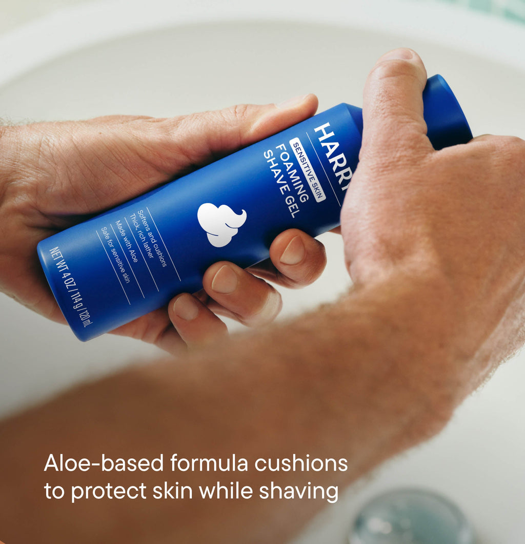 Hand holding a blue bottle of Harry's shaving gel with text about aloe-based formula.