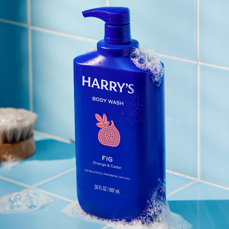 Blue bottle of Harry's body wash with a pump on a tiled bathroom floor.