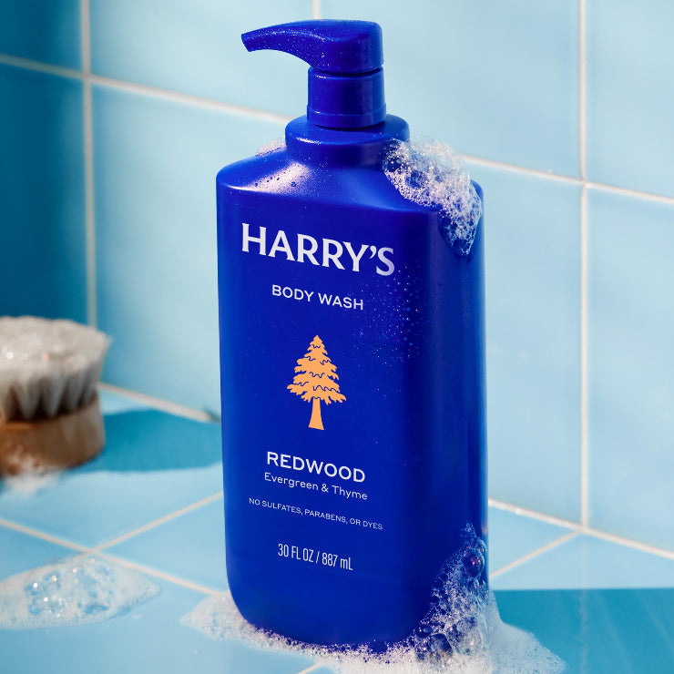 Blue bottle of Harry's Redwood body wash on a tiled bathroom shelf.