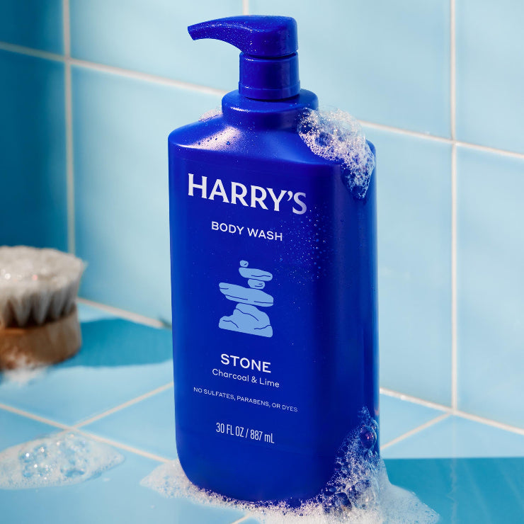 Blue bottle of Harry's body wash on a tiled bathroom floor