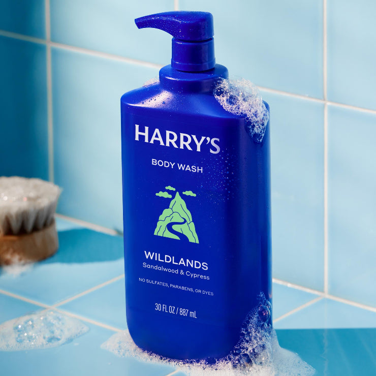 Blue bottle of Harry's Wildlands body wash on a tiled bathroom shelf.