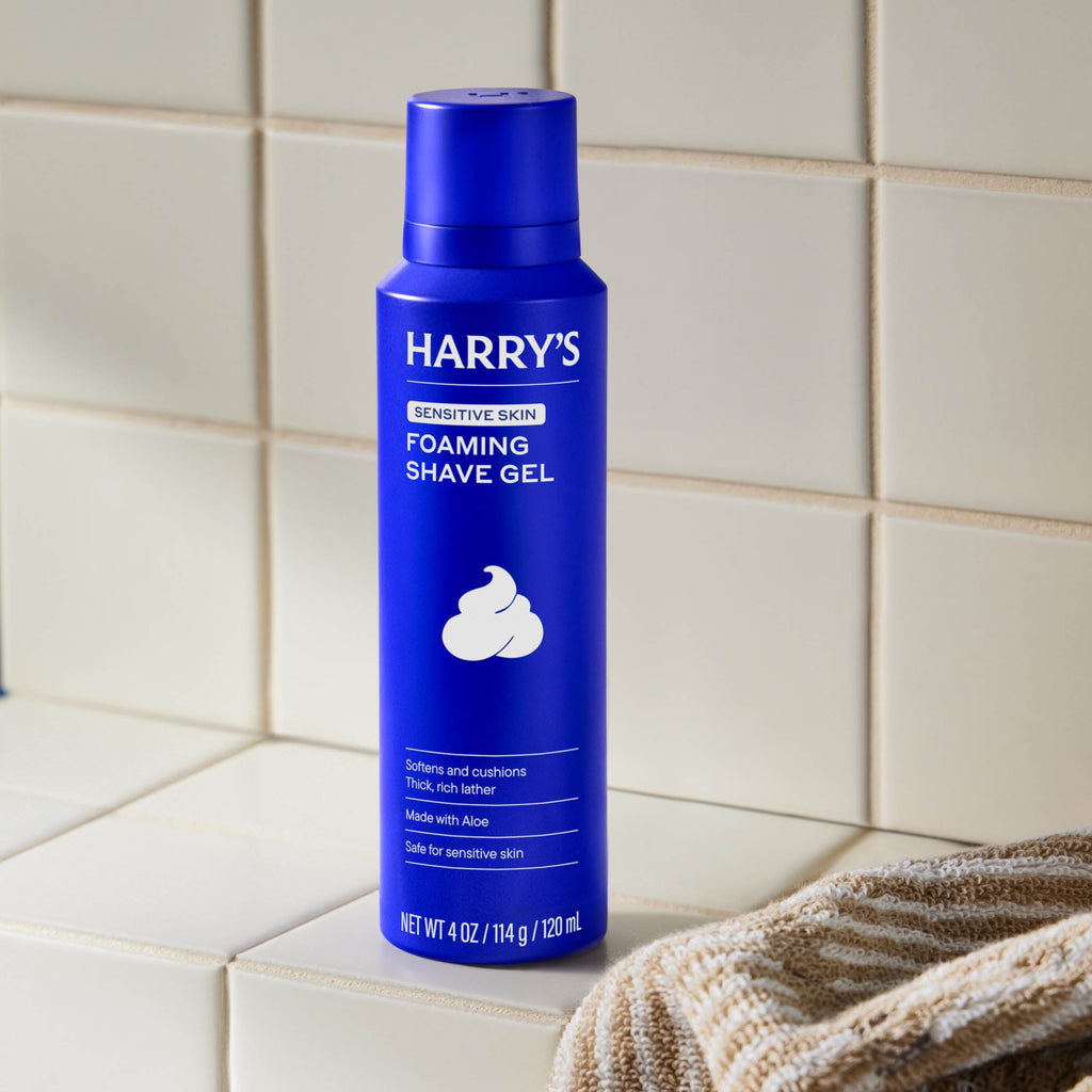 Blue bottle of Harry's foaming shave gel on a tiled bathroom counter.