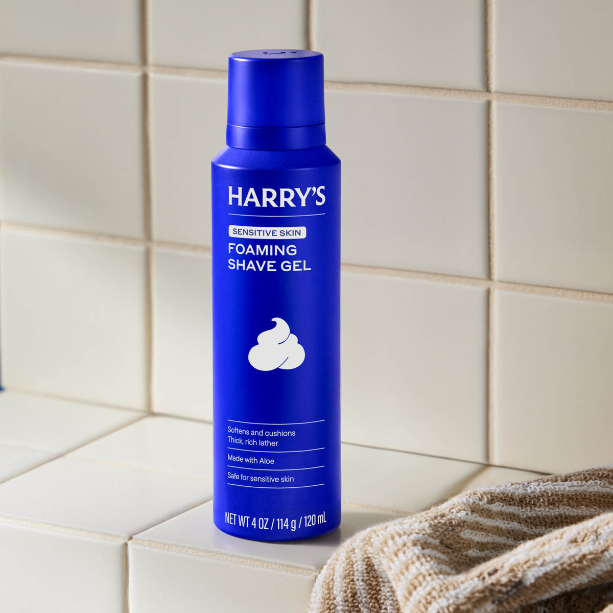 Blue bottle of Harry's foaming shave gel on a tiled bathroom counter.