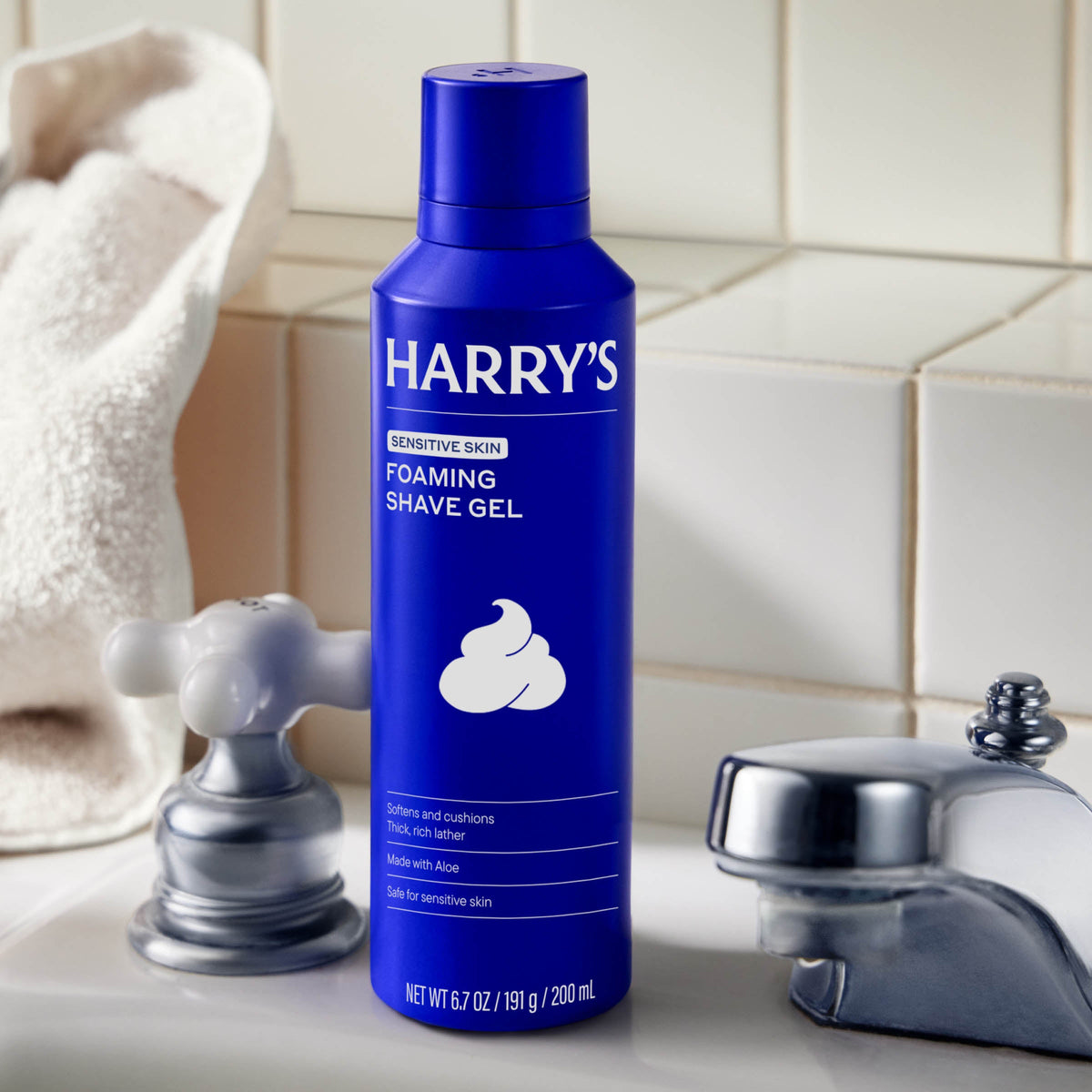 Blue bottle of Harry's foaming shave gel on a bathroom counter with a tiled wall background.