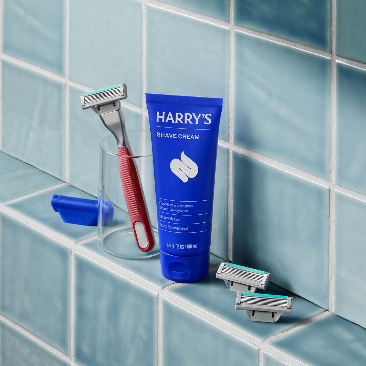 Harry's shave cream tube and razors on a tiled bathroom shelf