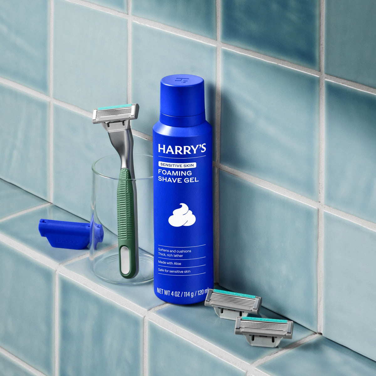 Blue bottle of Harry's foaming shave gel with a razor on a tiled bathroom shelf.