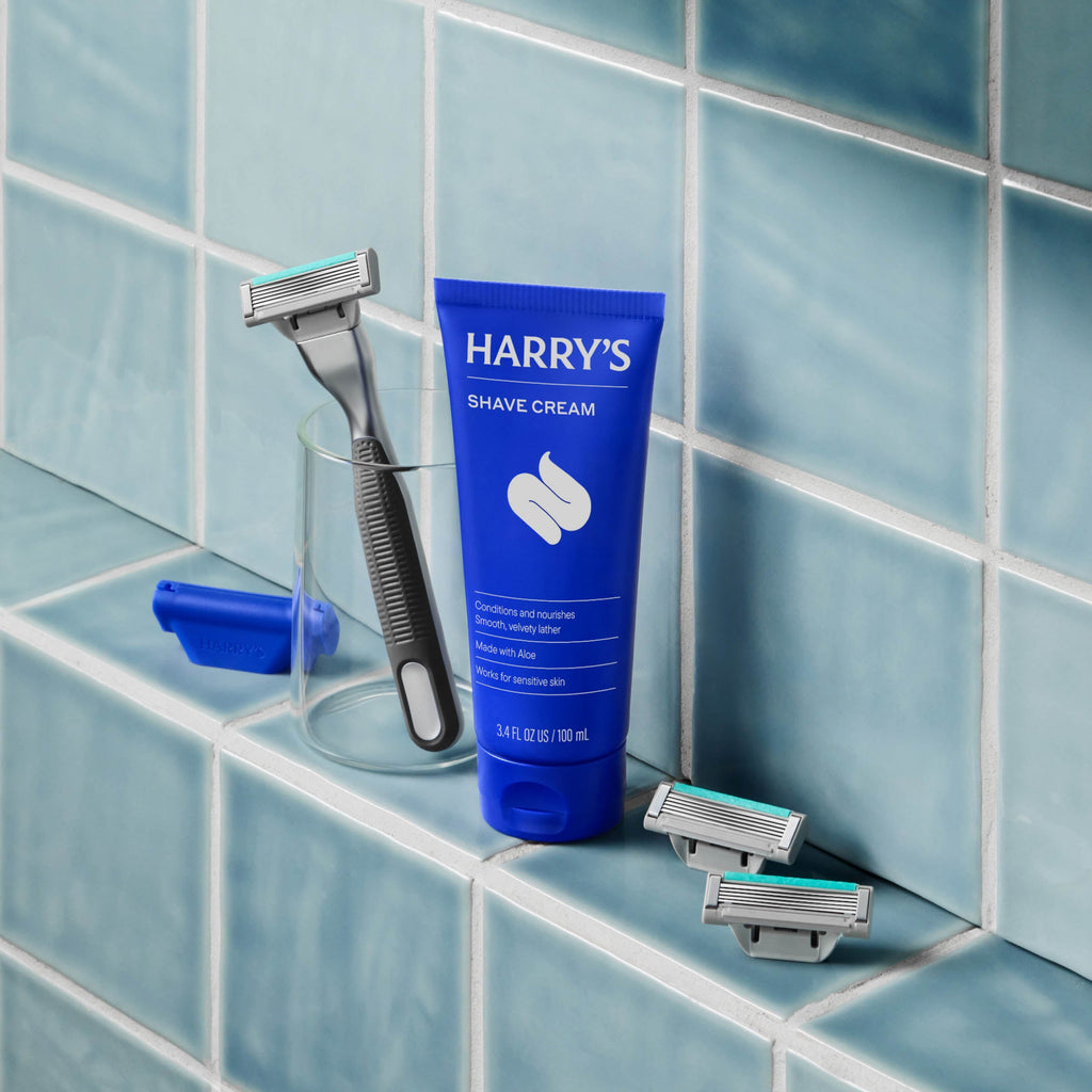 Harry's shave cream tube and razors on a tiled bathroom shelf
