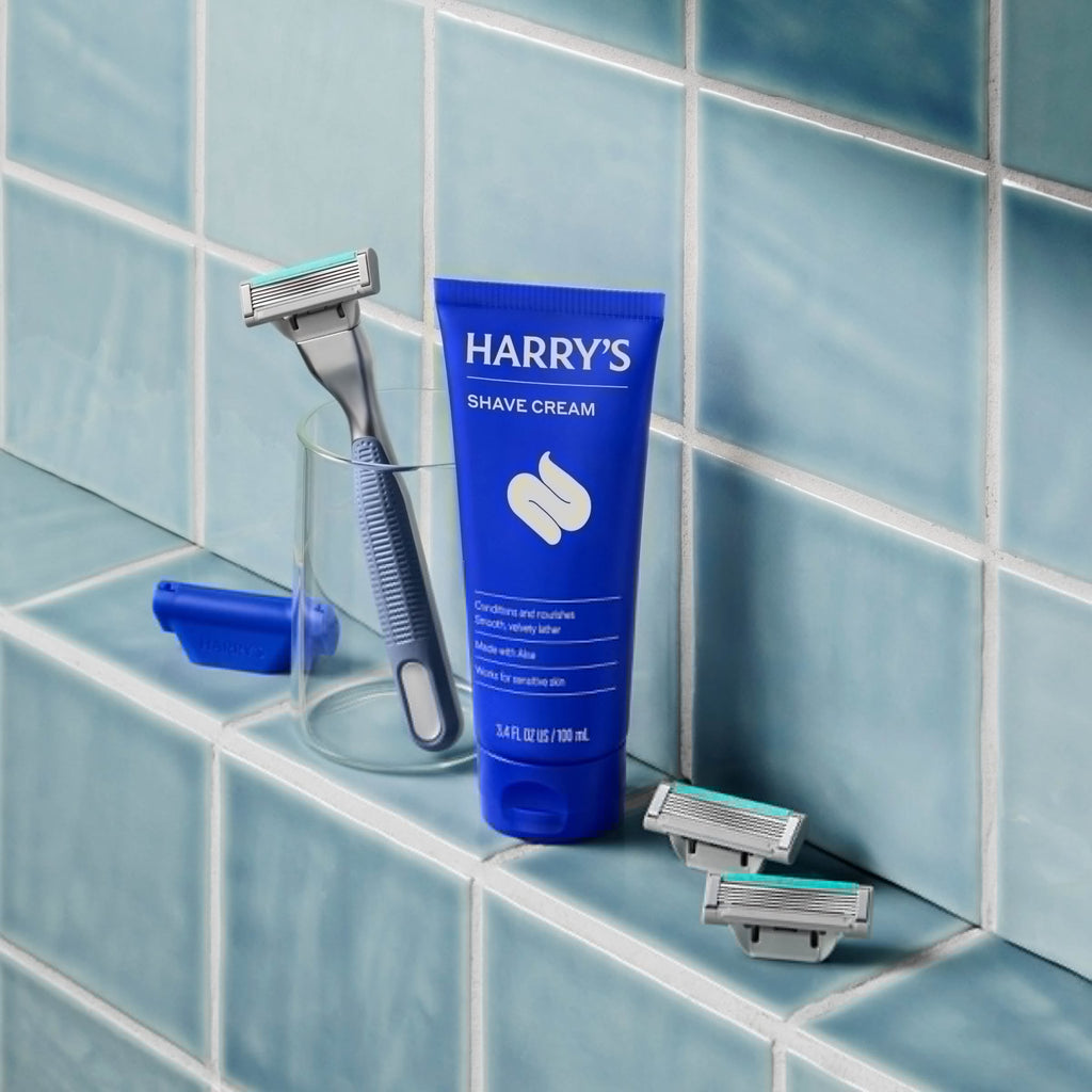Harry's shave cream tube and razors on a tiled bathroom shelf