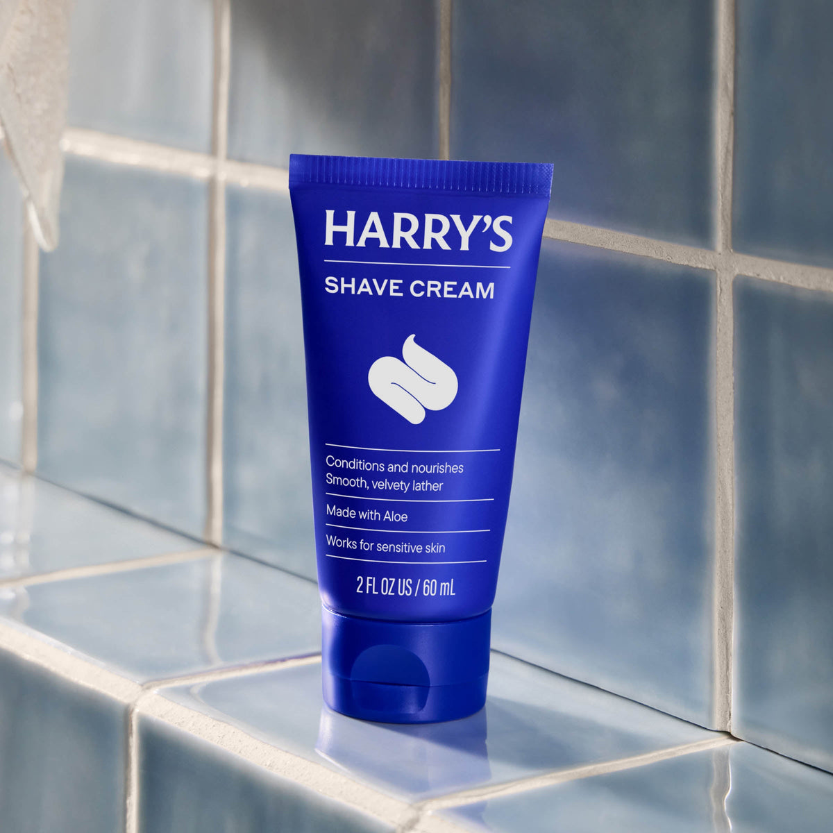 Blue tube of Harry's Shave Cream on a tiled bathroom shelf