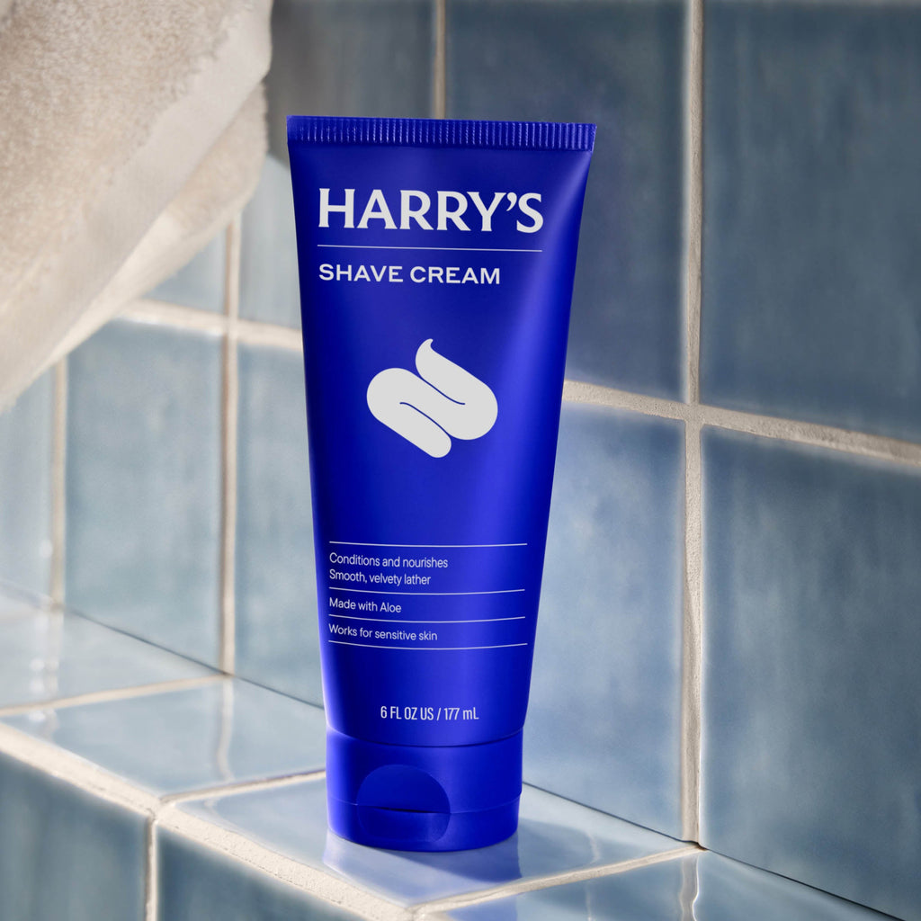 Blue tube of Harry's Shave Cream on a tiled bathroom shelf