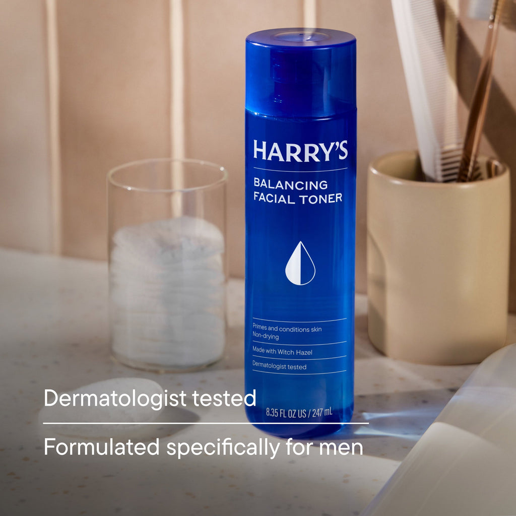 Blue bottle of Harry's Balancing Facial Toner on a bathroom counter with cotton pads and a glass.