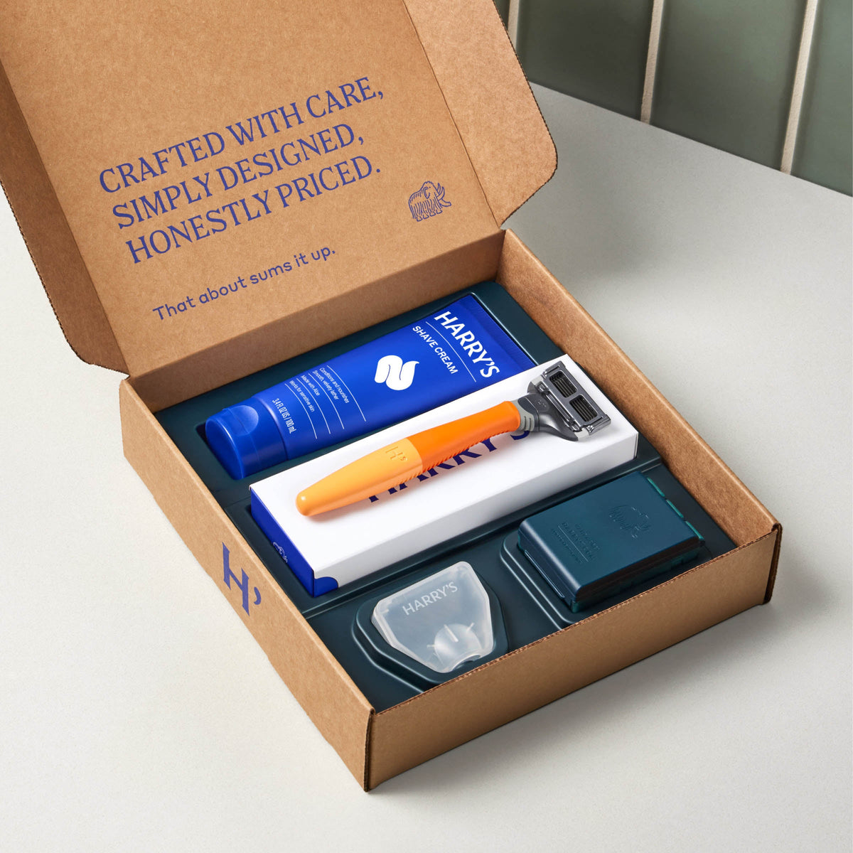 Harrys's grooming kit with a razor, cream, and other items in an open cardboard box.