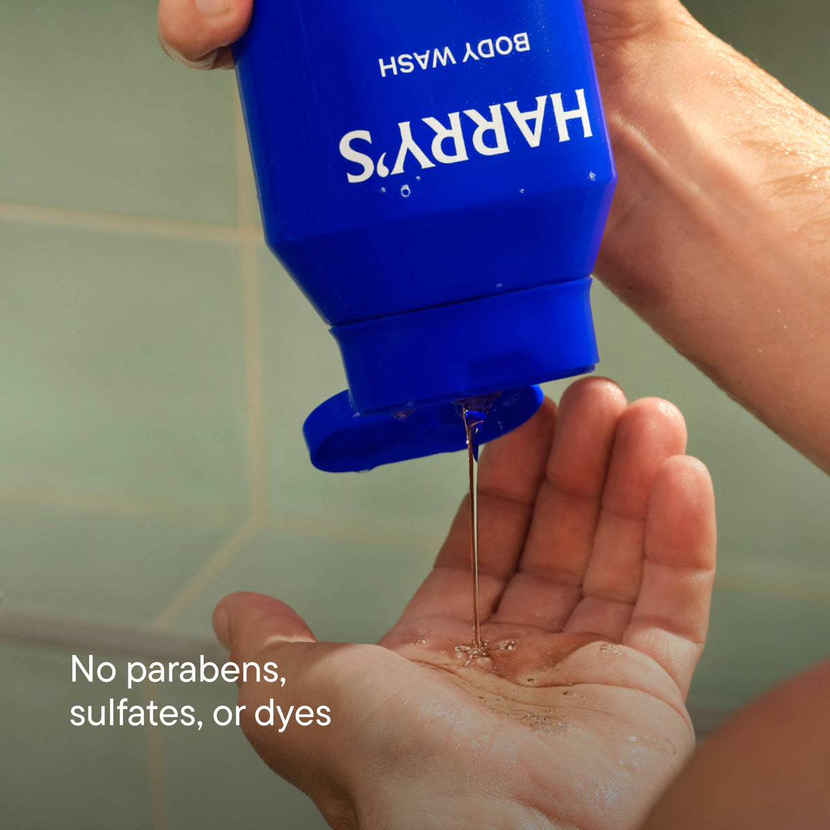 Hand holding a blue bottle of Harry's body wash with soap being dispensed.