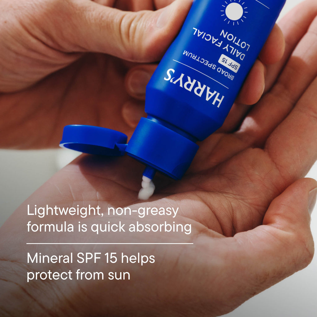 Hand holding a blue bottle of Harry's daily facial lotion with SPF 15.