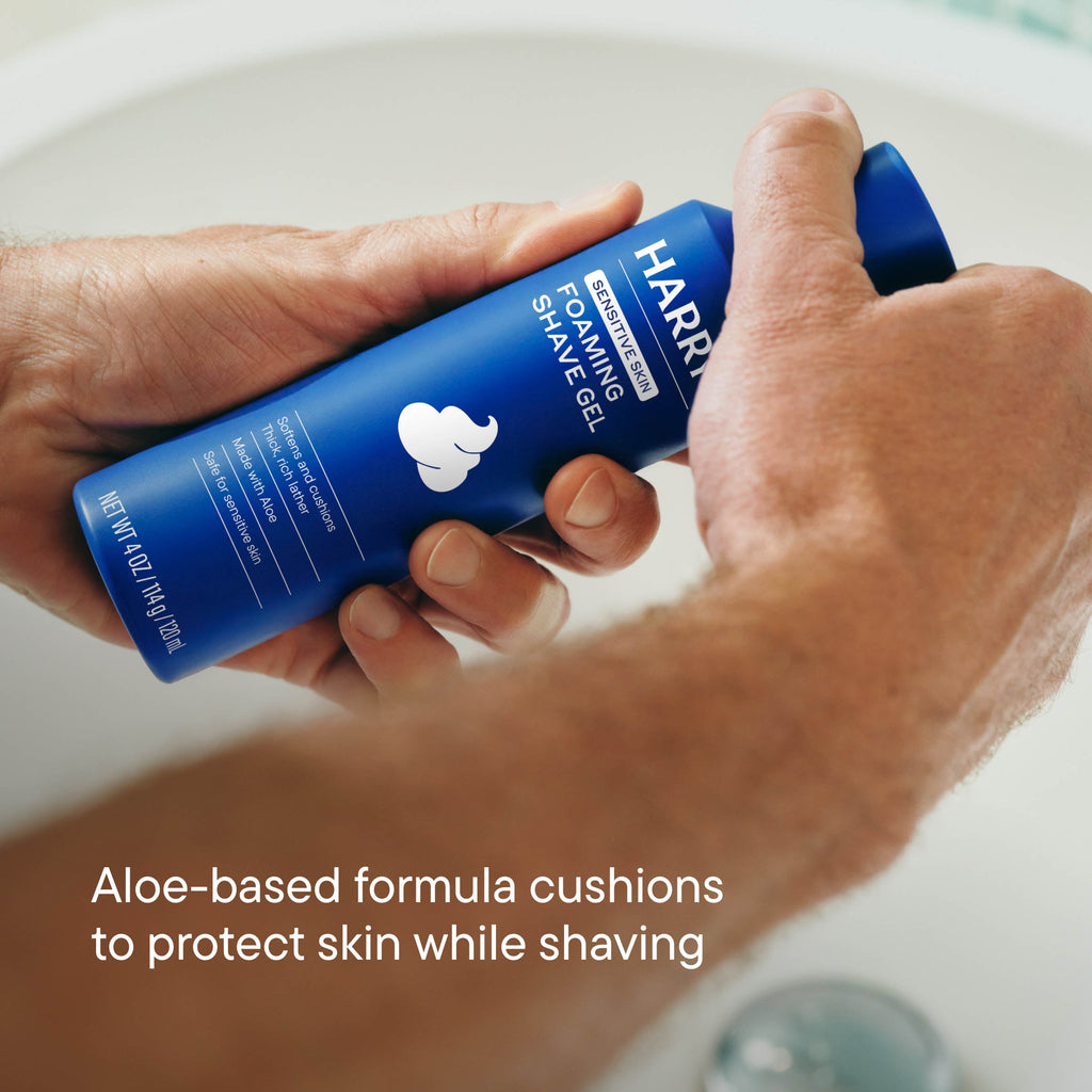 Hand holding a blue bottle of Harry's foaming shave gel with a sink in the background.