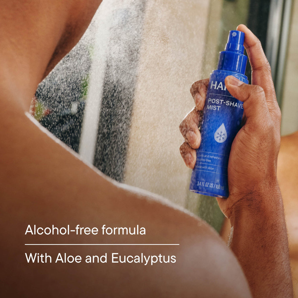 Person holding a blue post-shave mist bottle with shower in background