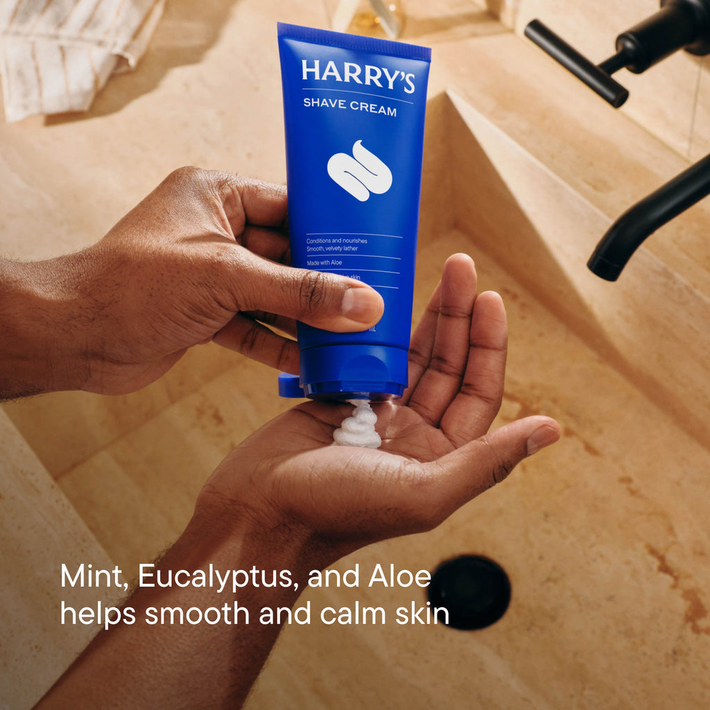 Hand holding a tube of Harry's Shave Cream with a bathroom background