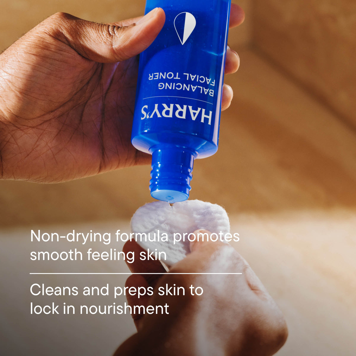 Hand holding a blue bottle labeled 'HARRY'S' with text about skincare benefits.