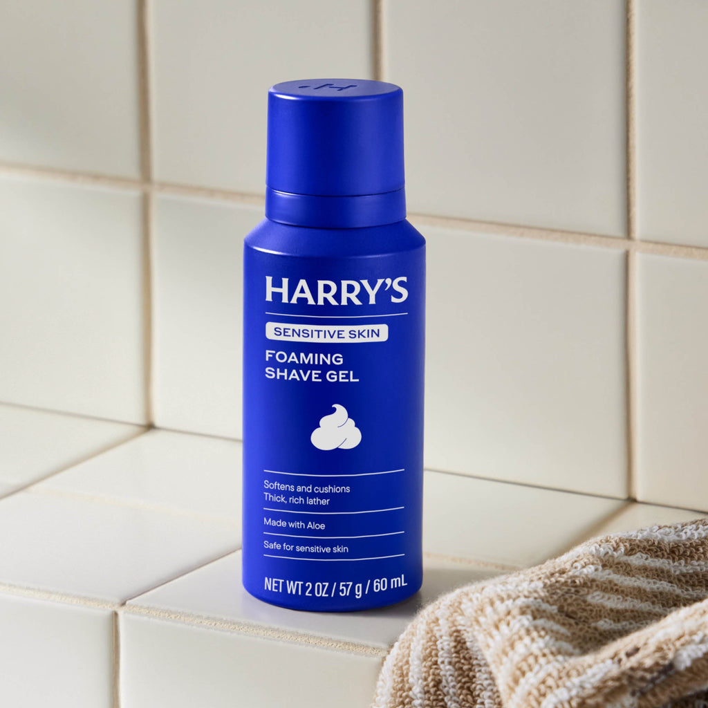 Blue bottle of Harry's foaming shave gel on a tiled bathroom shelf