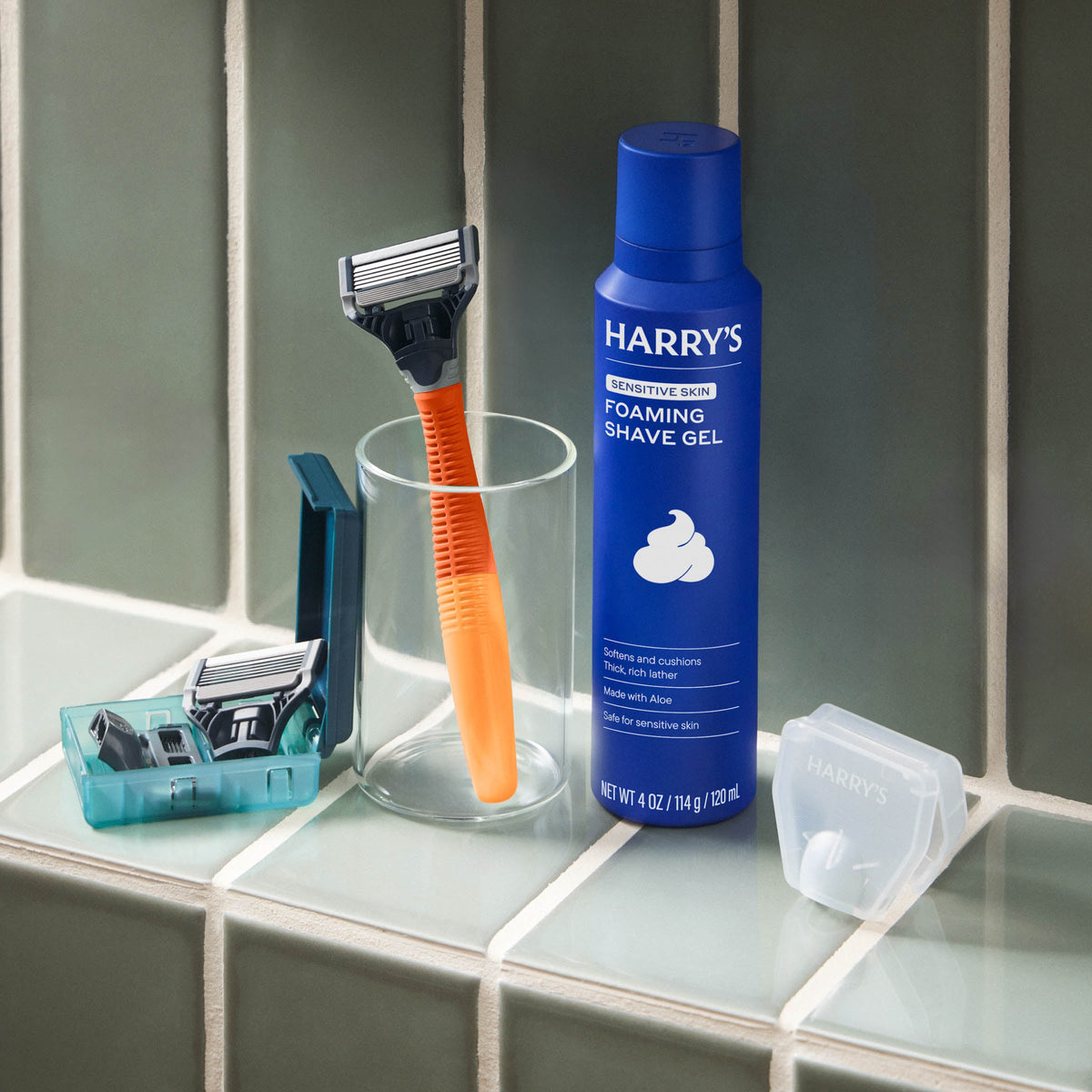 Harry's shaving products including a blue foaming shave gel bottle, orange razor, and razors in a holder on a bathroom counter.