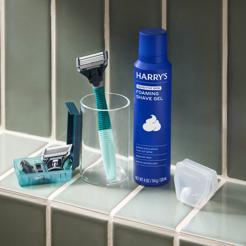 Harry's shaving products including a blue bottle of foaming shave gel, a razor, and razors in a holder on a bathroom counter.