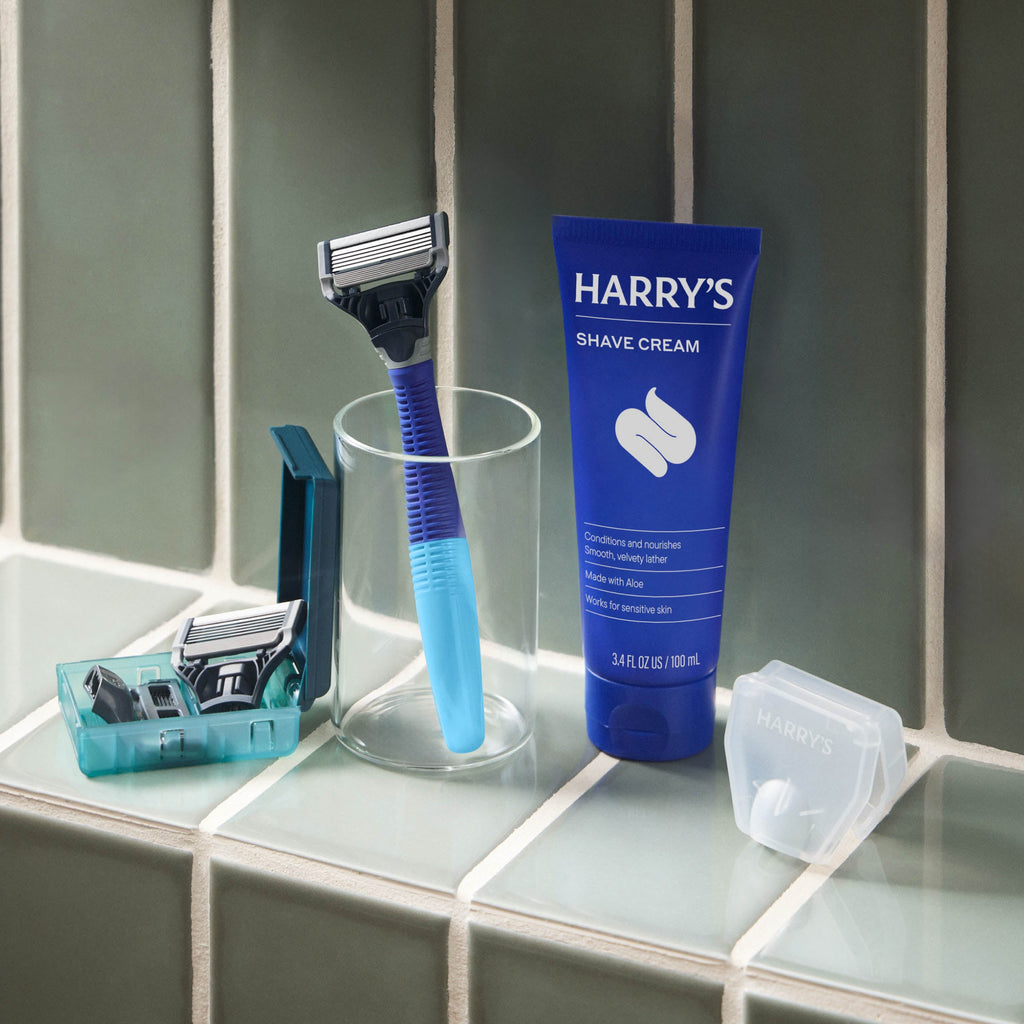 Shaving products including a razor, razor heads, and a tube of Harry's shave cream on a bathroom counter.