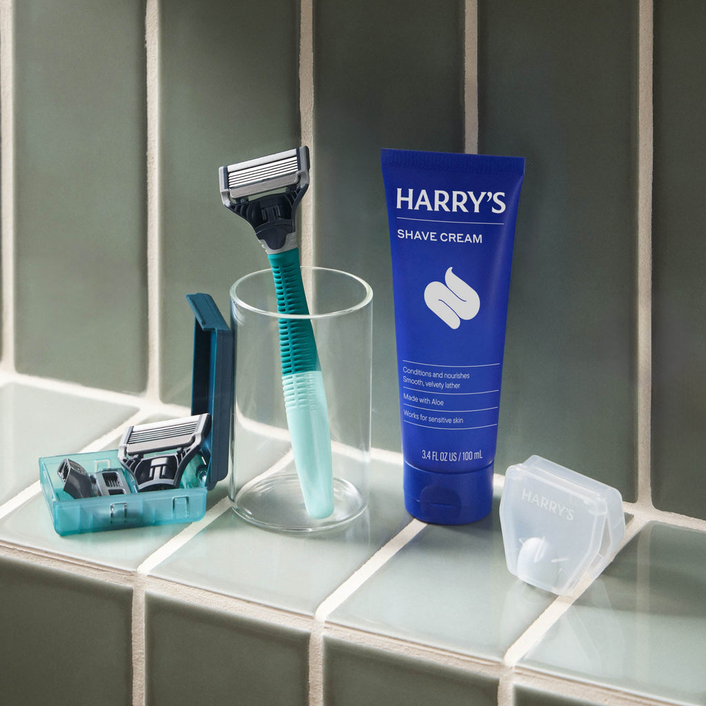 Shaving products including a razor, cup, and tube of Harry's shave cream on a bathroom counter.