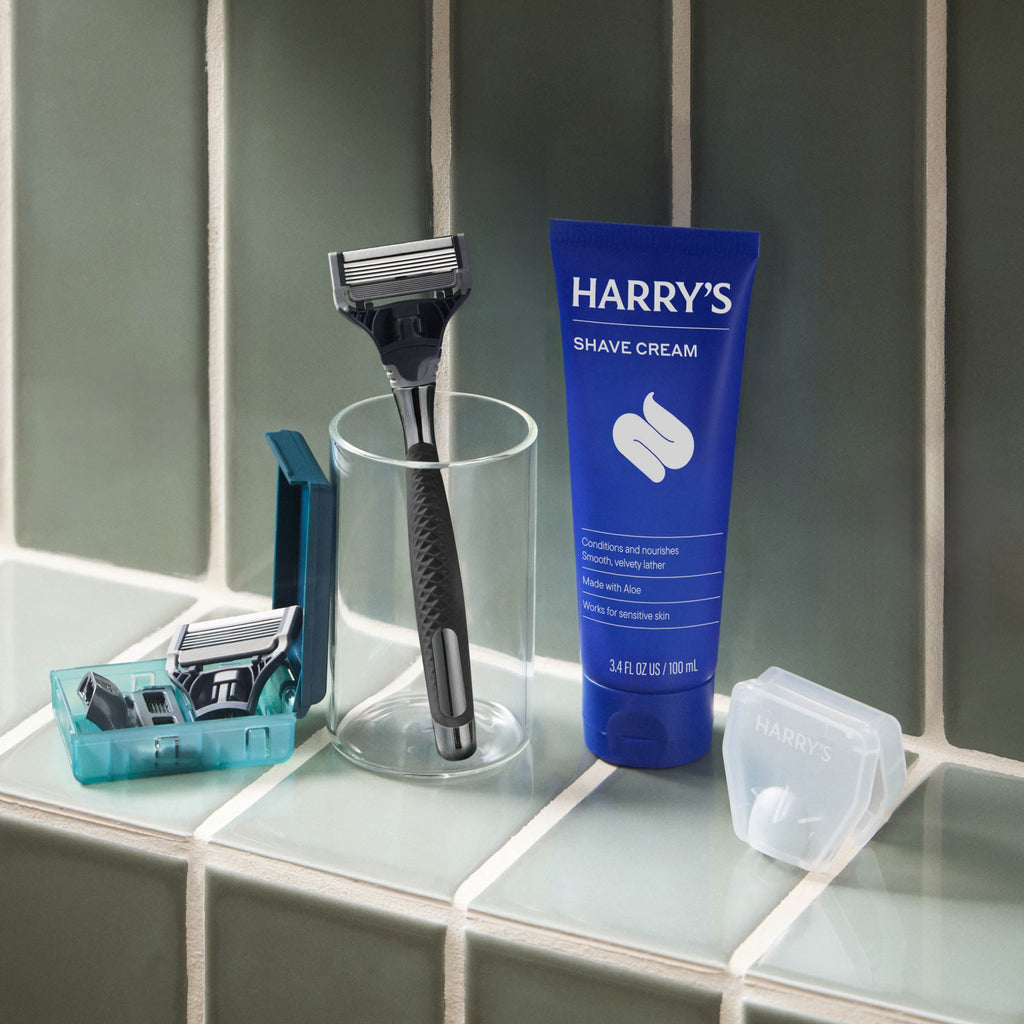Shaving kit with razor, razors in a container, and Harry's shave cream on a bathroom counter.