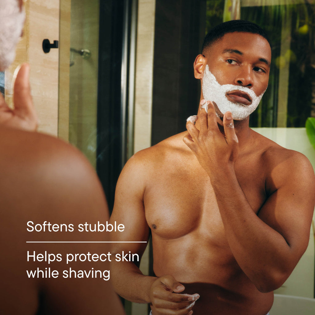 Man shaving his face with a product, standing in front of a mirror.