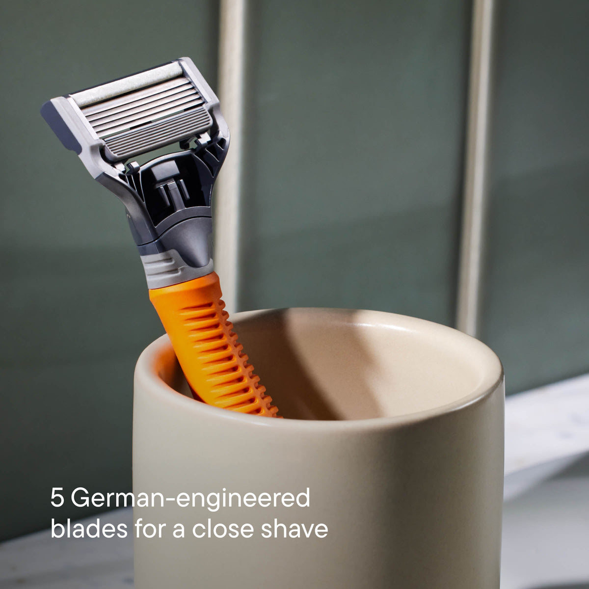 Shaving razor with orange handle in a cup against a neutral background