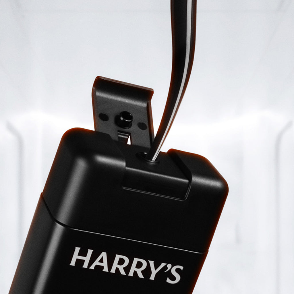 Close-up of a black HARRY'S branded Dark Matter body wash with a visible stream of the body wash leaving the top opening, photographed against a soft white background.