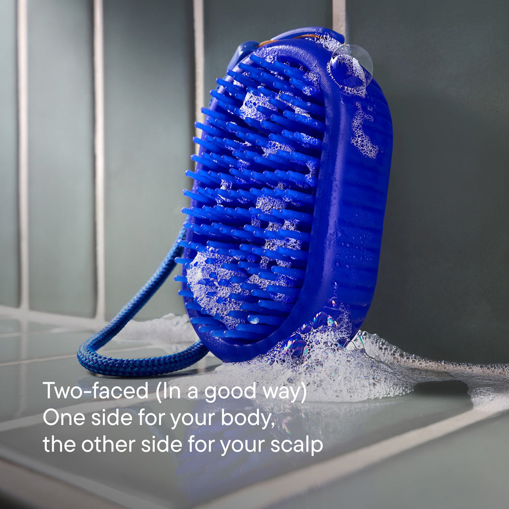 Blue scrubber with bristles and a handle on a tiled surface, with text describing its dual use for body and scalp.