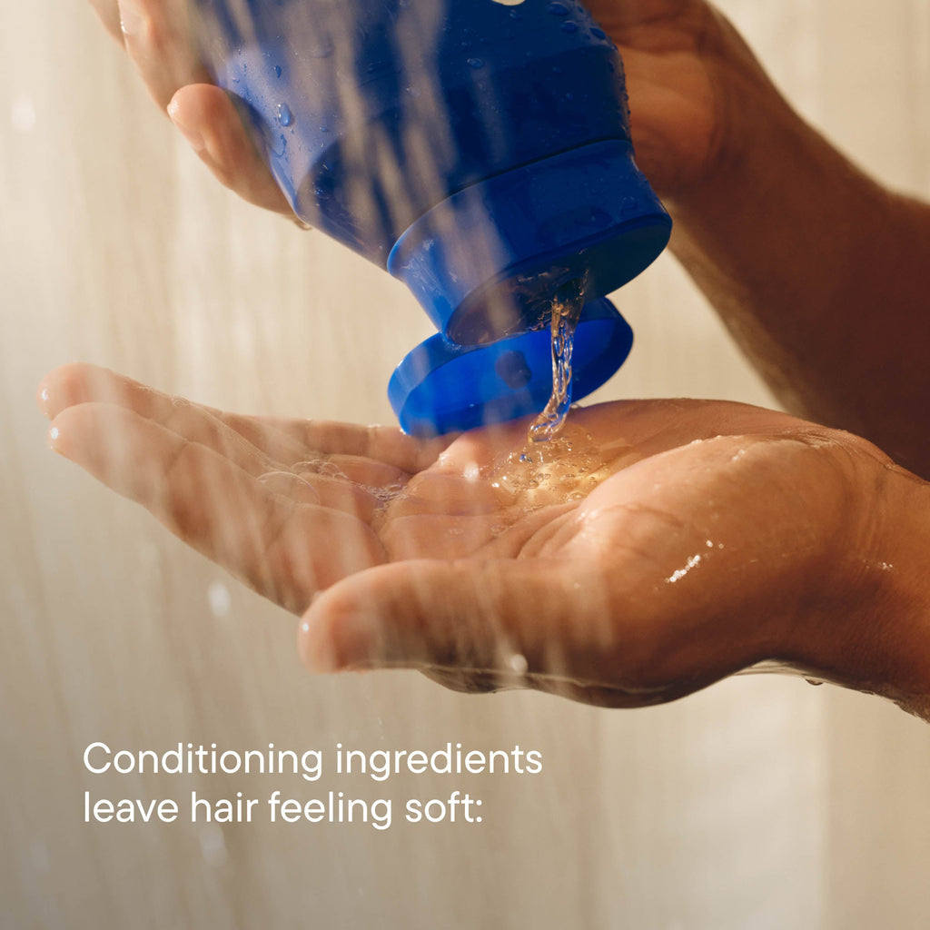 Hand holding a blue bottle with liquid being poured onto it, against a neutral background.