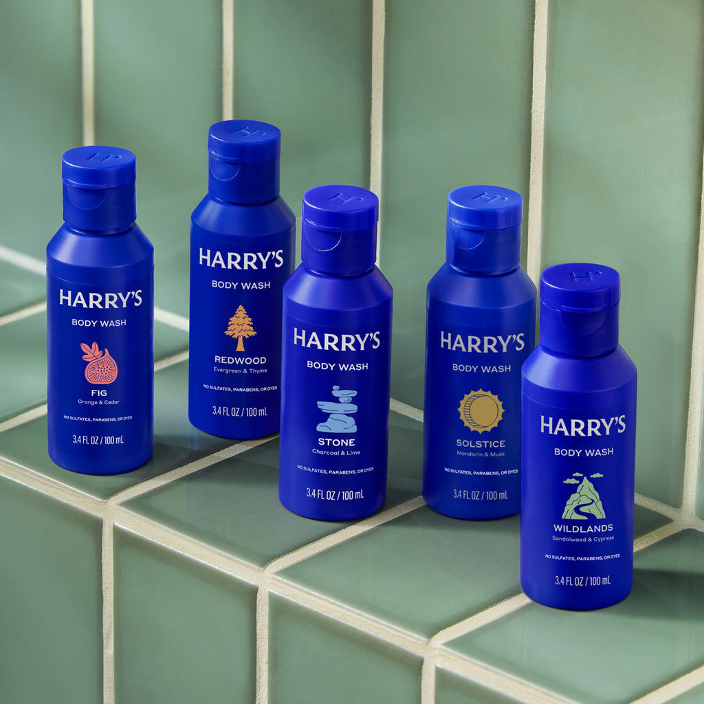 Five bottles of Harry's body wash on a tiled bathroom floor.