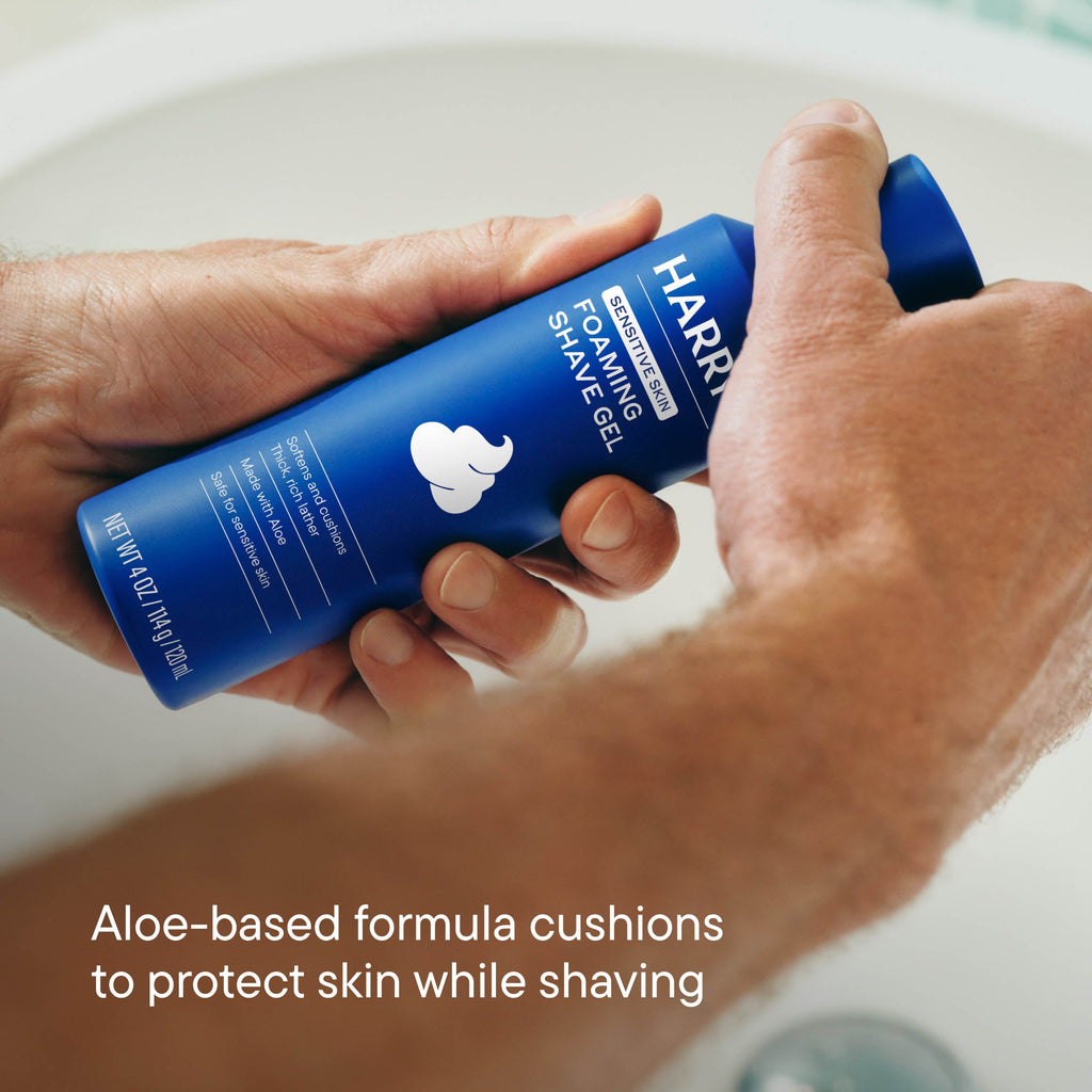Hand holding a blue bottle of Harry's shaving gel with text about aloe-based formula.