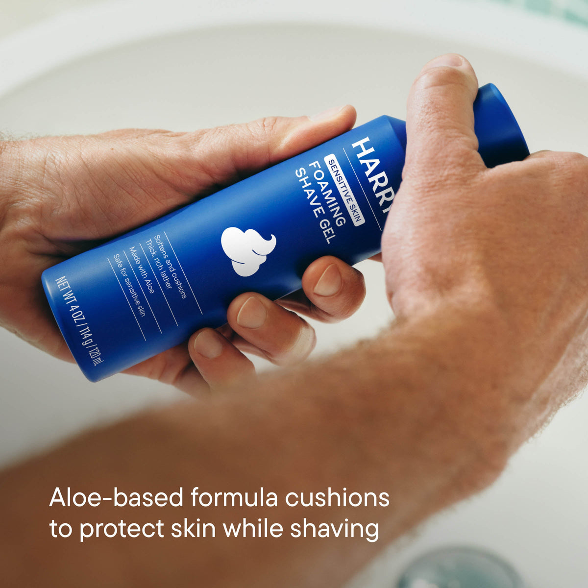 Hand holding a blue bottle of Harry's shaving gel with text about aloe-based formula.